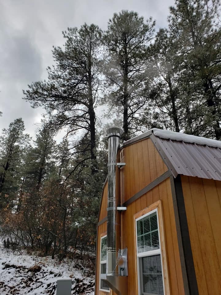 Cedar-sided cabin exterior with the wood stove chimney and snow on the metal roof