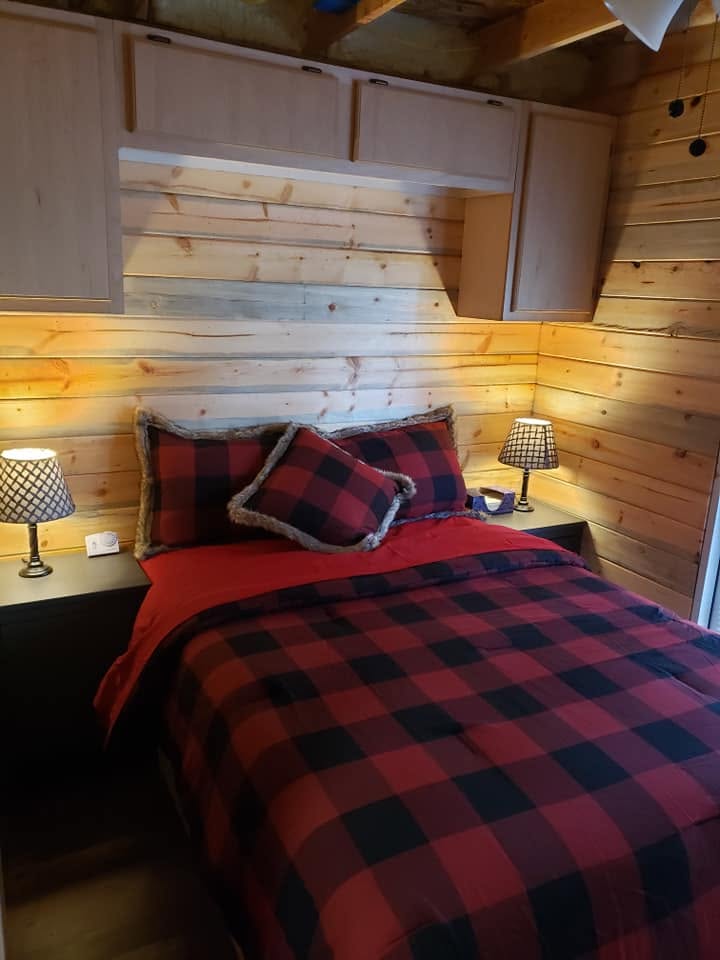 Bedroom bed with plaid pillows, overhead pine cabinets and matching lamps