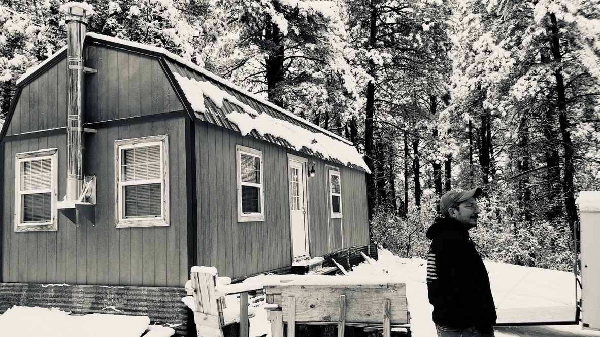 Snow-covered cabin in the pines with the wood stove chimney